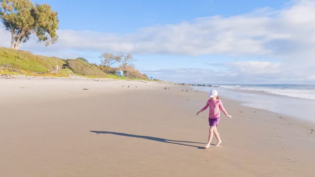 A little girl joyfully plays on the vast, empty sands of El Capitan State Beach in California during winter.