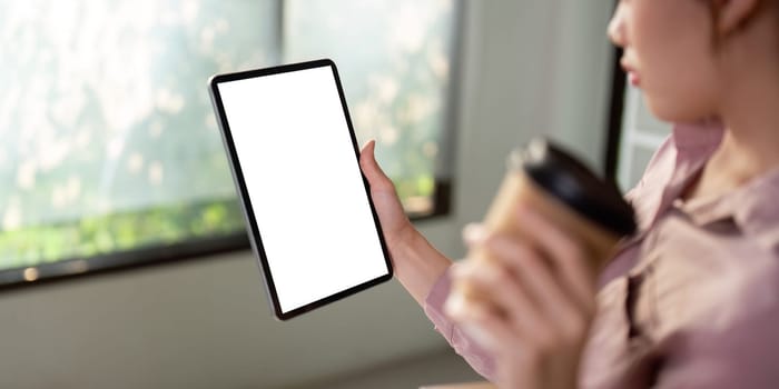 Mockup of a woman holding digital tablet with blank white desktop screen with holding a coffee cup.