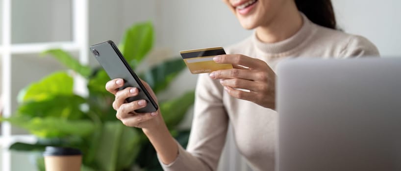 Young woman holding credit card using smartphone payment at home. Female customer shopping making purchase online on smartphone.