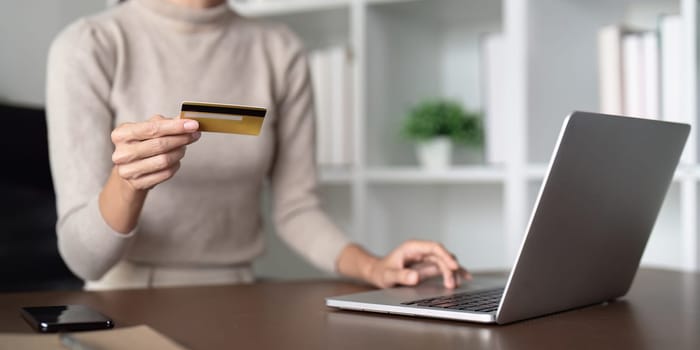 Young woman holding credit card using laptop payment at home. Female customer shopping making purchase online on laptop.