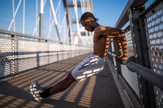 Young a man is exercising on the bridge in the city. He is doing reverse push-ups.
