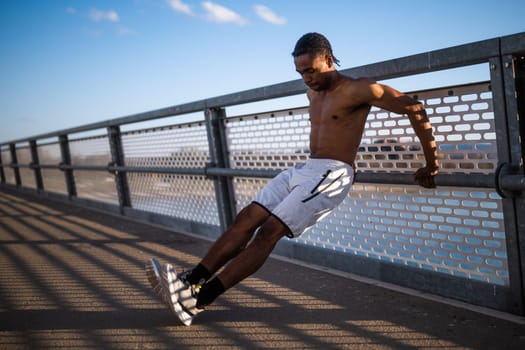 Young  man is exercising on the bridge in the city. He is doing reverse push-ups.