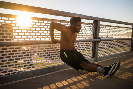 Young  man is exercising on the bridge in the city. He is doing reverse push-ups.