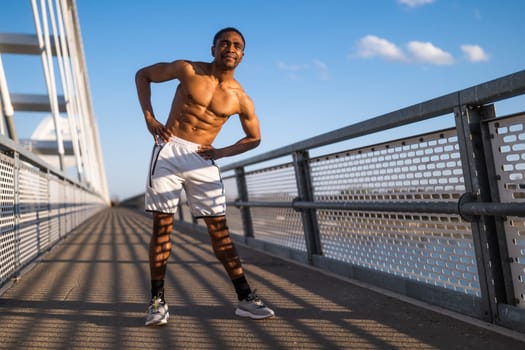 Young man is exercising on the bridge in the city. He is stretching his body.