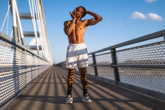 Young man is exercising on the bridge in the city. He is stretching his body.