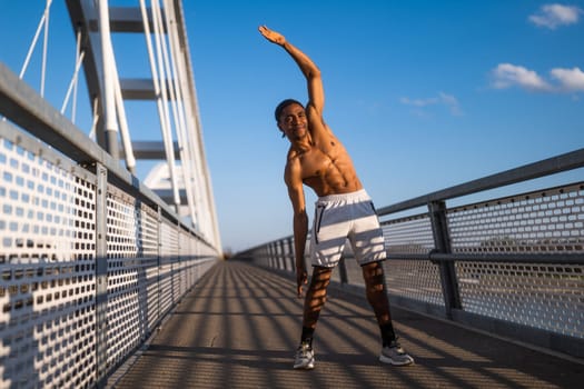Young  man is exercising on the bridge in the city. He is stretching his body.