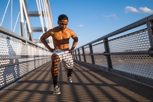 Young man is exercising on the bridge in the city. He is stretching his body.