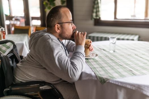 Paraplegic handicapped man in wheelchair is sitting at restaurant and drinking coffee.