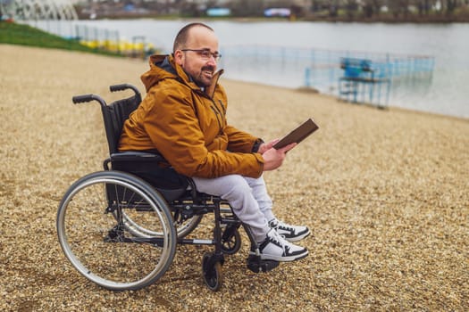 Paraplegic handicapped man in wheelchair is reading book outdoor.
