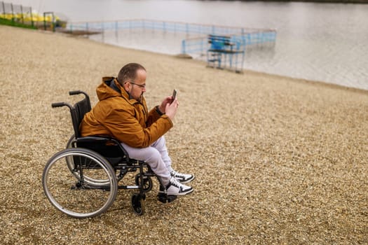 Paraplegic handicapped man in wheelchair is messaging on smartphone outdoor.