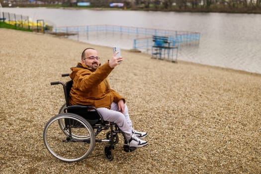 Paraplegic handicapped man in wheelchair is taking selfie with smartphone outdoor.