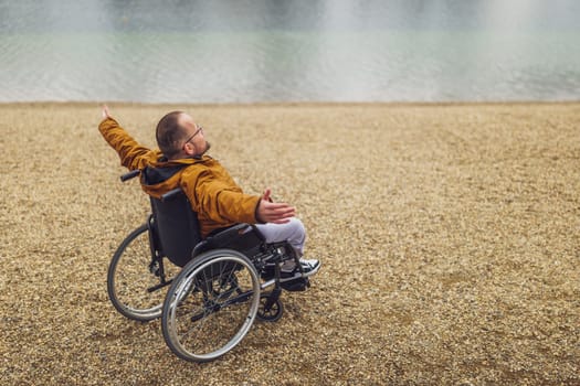 Rear view image of paraplegic handicapped man in wheelchair by the lake. He is enjoying outdoor.