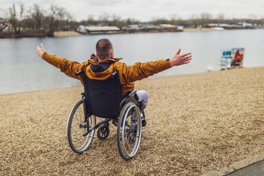 Rear view image of paraplegic handicapped man in wheelchair by the lake. He is enjoying outdoor.