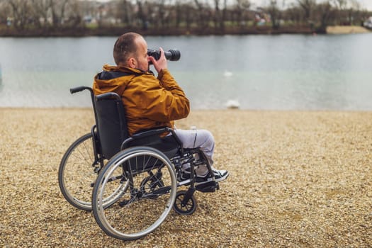 Paraplegic handicapped man in wheelchair is photographing outdoor.