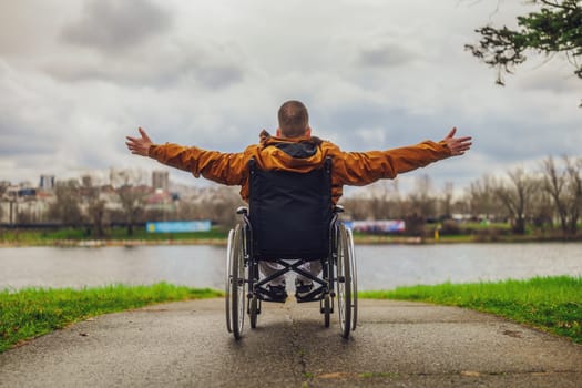 Rear view image of paraplegic handicapped man in wheelchair by the lake. He is enjoying outdoor.