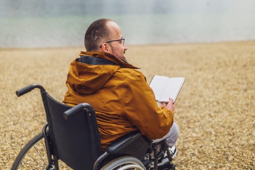 Paraplegic handicapped man in wheelchair is reading book outdoor.