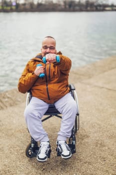 Happy paraplegic handicapped man in wheelchair by the lake. He is ready for exercise with weights.