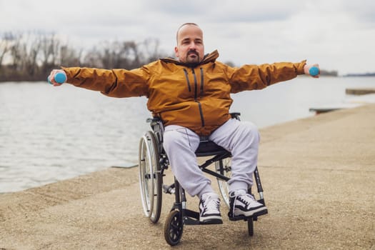 Paraplegic handicapped man in wheelchair by the lake. He is exercising with weights.