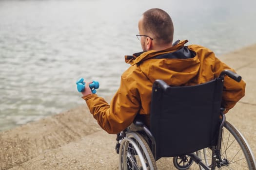 Paraplegic handicapped man in wheelchair by the lake. He is ready for exercise with weights.