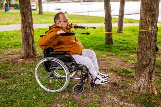 Paraplegic handicapped man in wheelchair is exercising with stretch band in park.