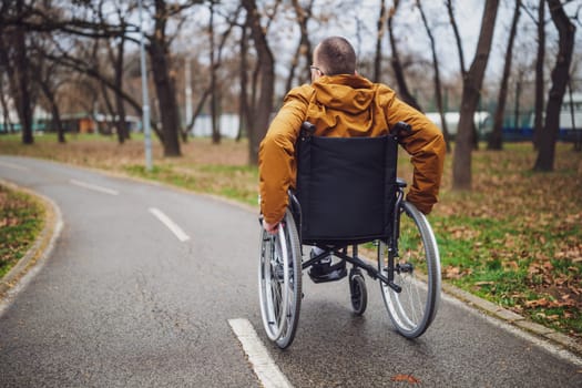 Rear view image of paraplegic handicapped man in wheelchair in park. He is rolling on pathway.