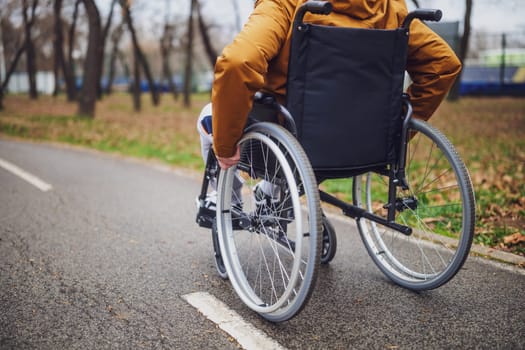 Close up image of paraplegic handicapped man in wheelchair in park. He is rolling on pathway.