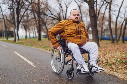 Portrait of happy paraplegic handicapped man in wheelchair in park. He is rolling on pathway.