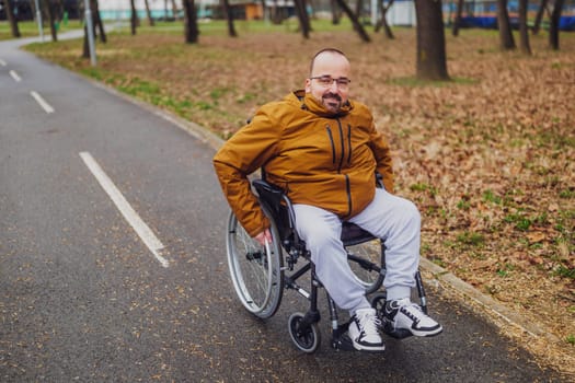 Portrait of happy paraplegic handicapped man in wheelchair in park. He is rolling on pathway.
