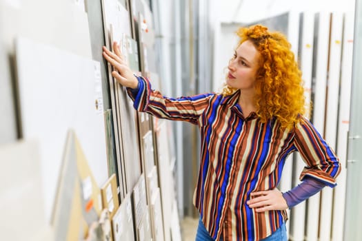 Portrait of buyer in bathroom store. Redhead woman is choosing tiles for her apartment.