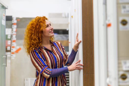 Portrait of buyer in bathroom store. Redhead woman is choosing tiles for her apartment.