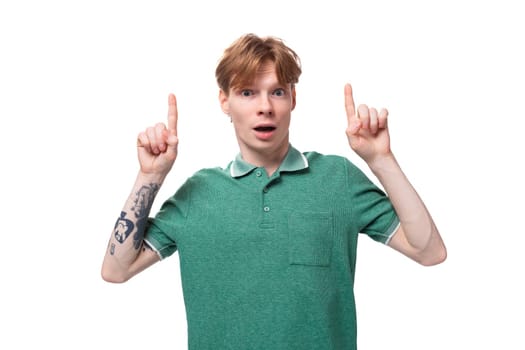 young satisfied happy european guy with red hair with a tattoo on his forearm points his finger at the space for advertising.