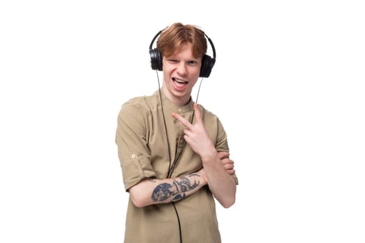 young red-haired man with glasses dressed in a brown shirt grimaces and listens to music on headphones.