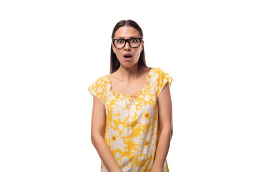 young woman dressed in a yellow sundress and with glasses for vision is surprised on a white background.