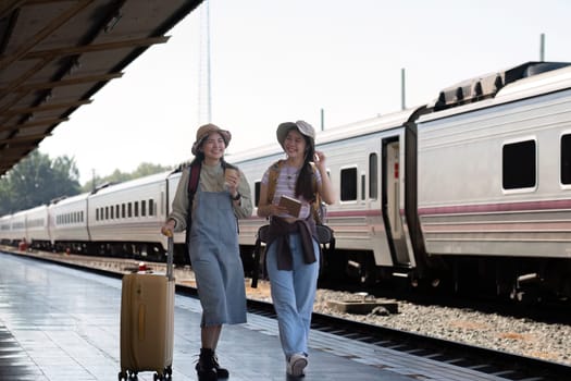 Two Asian female tourist friends are at the train station. Waiting for the train to travel to the provinces together on the weekend..