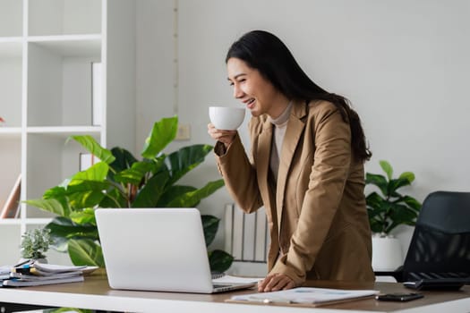 smiling businesswoman drinking coffee and working on laptop in green modern office. Nice Environment Office. Eco-Friendly Concept.