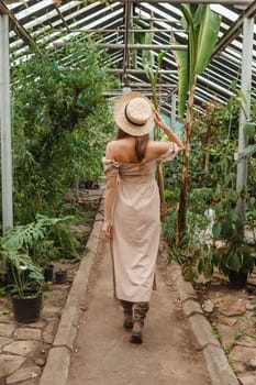 A beautiful young woman takes care of plants in a greenhouse. The view from the back. Concept of gardening and an eco-friendly lifestyle.