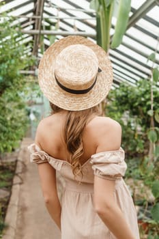 A beautiful young woman takes care of plants in a greenhouse. The view from the back. Concept of gardening and an eco-friendly lifestyle.