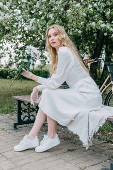 A blonde girl with long hair on a walk in a spring park. Springtime and blooming apple trees