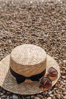 A straw hat and sunglasses on the beach. Pebbles on the seashore, close-up. The natural background