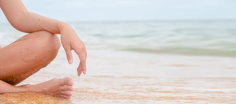 Panoramic close-up image of the legs and arms of a Caucasian young woman. Sits relaxing in lotus position on the seashore.