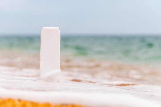 A bottle of sunscreen without a label on the beach on a sunny day. Blank for advertising your cream and labels.