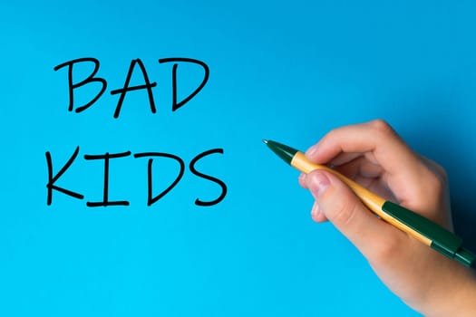 Children hand with pen write on a blue white background. Writing hand. Word Bad kids