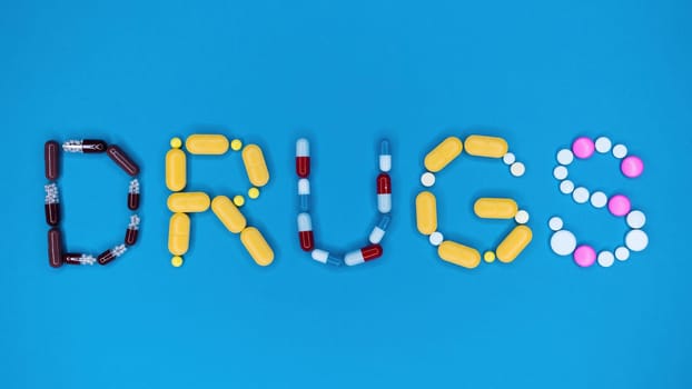 Multicolored capsules in word drugs. Blue background. Pharmacy, antidepressants, medicine concept. High quality photo