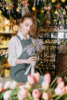 A woman in her florist shop collects bouquets of flowers. The concept of a small business. Bouquets of tulips for the holiday on March 8