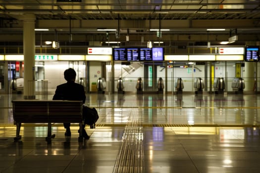 A man sits on a bench in a train station..