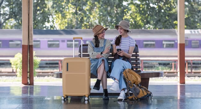 Two Asian female tourist friends are at the train station. Waiting for the train to travel to the provinces together on the weekend..