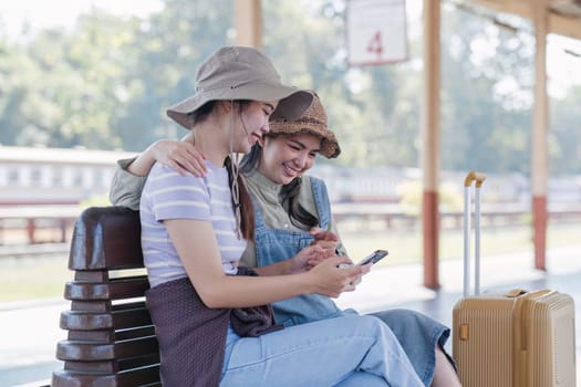 Two Asian female tourist friends are at the train station. Waiting for the train to travel to the provinces together on the weekend..