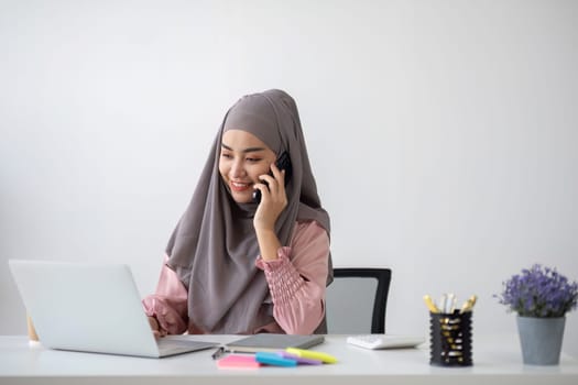 Smiling Muslim business woman Wearing a hijab while chatting online on a work desk in the office..