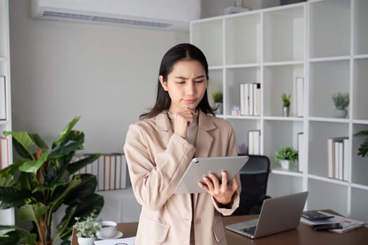 Unhappy Asian business woman shows stress over unsuccessful business while working in home office decorated with soothing green plants..