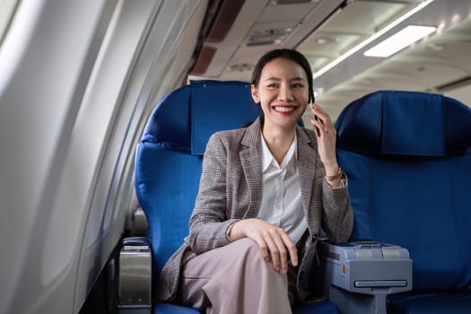 Young woman talking on the phone, communicating on business before traveling Sitting near window in first class on airplane during flight, travel and business concept..